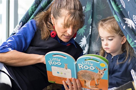 An educator reading a book with a child in a child's teepee