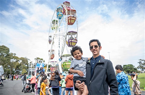 Parent holding a young child at a fair with amusement rides